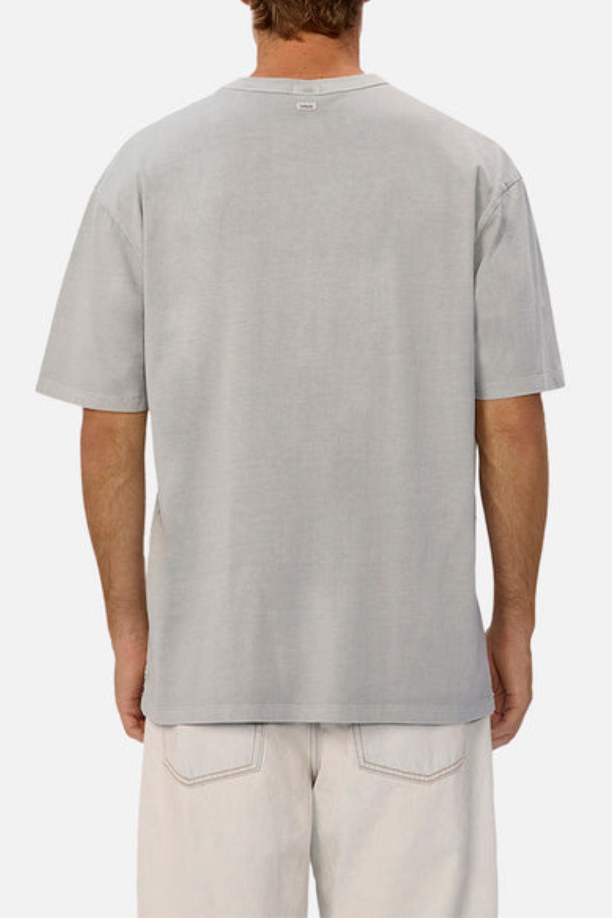 A person is seen from the back wearing an oversized Industrie The Del Sur Tee in light gray heavyweight fabric, paired with off-white pants featuring visible back pockets, standing against a plain white background.