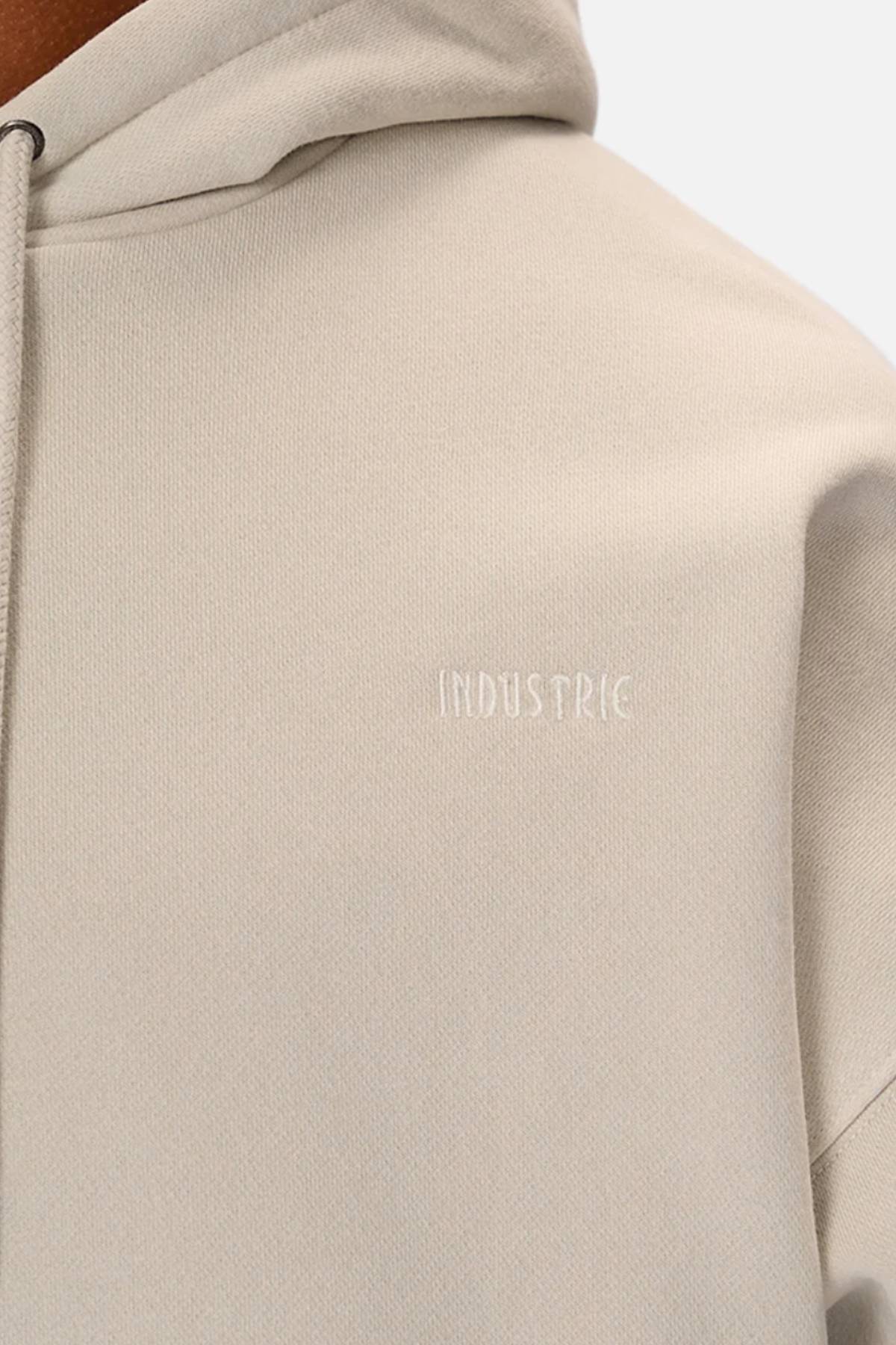 Close-up of the Industrie The Del Sur Washed Hoodie in light beige with "INDUSTRIE" subtly embroidered in white on the chest. Features a drawstring, visible shoulder seams, and an oversized fit for comfort.