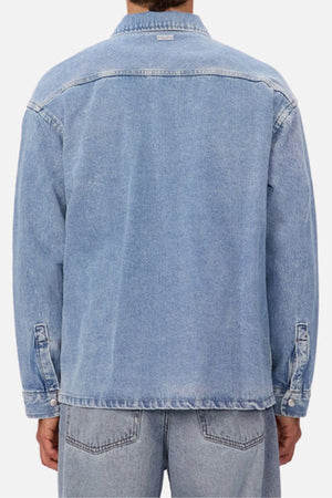 A person wearing the Industrie The Denim Overshirt in relaxed light blue denim with matching jeans, shown from the back against a plain white background for a cool vintage vibe.