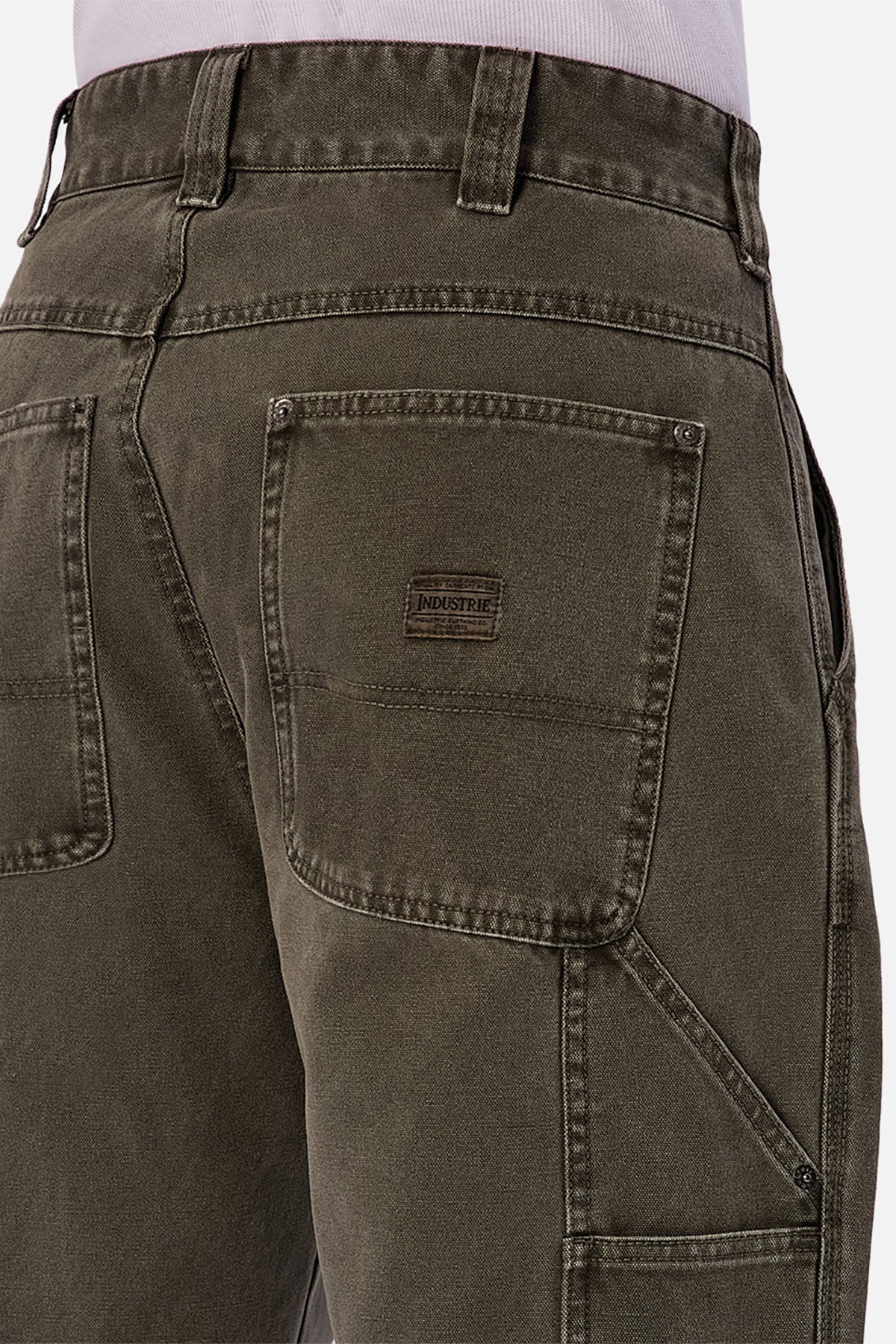Close-up of the back of a person wearing Industrie The Detroit Carpenter Pant in olive green 100% cotton canvas, featuring large back pockets and a small INDUSTRIE label, styled with a tucked-in white shirt for a street-style look.