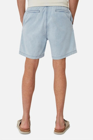 A person wearing Industrie The Dublin Short in light blue denim and flip-flops faces away from the camera. The shorts, celebrated for their breathable fit and two back pockets, are displayed against a plain white background.