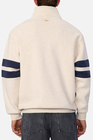 Someone wearing the Industrie The East Village Track Top in cream with navy stripes on both sleeves, seen from behind. This relaxed-fit, high-collar jacket is styled with faded black jeans for a fashionable casual look.