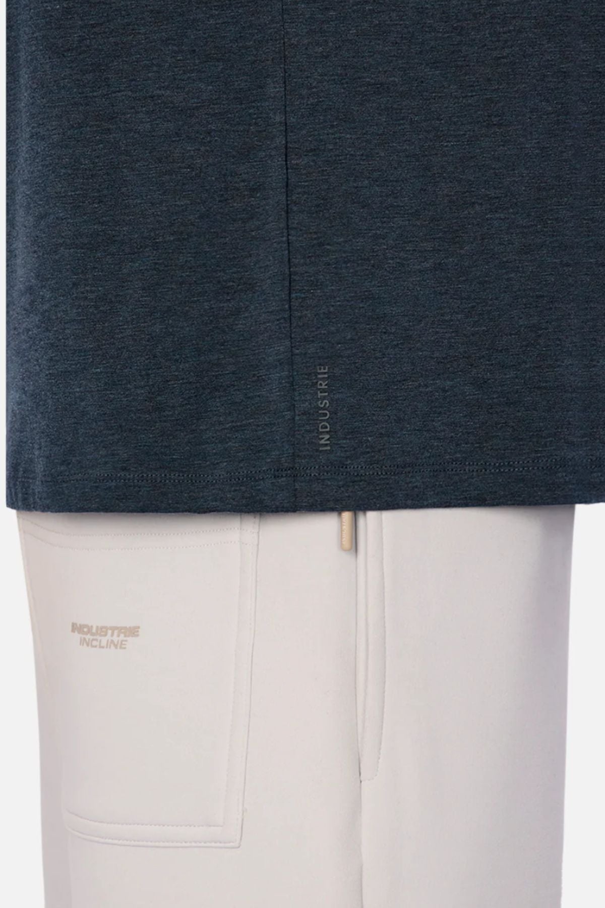 Close-up of a person in the relaxed fit Industrie The Freeman Athletic Tee in dark blue, styled with light beige pants. Subtle "INDUSTRIE INCLINE" branding and a visible pocket stand out, with the lightweight tee set against a plain white background.