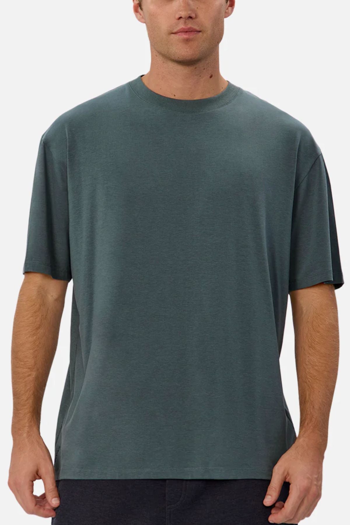A man wearing the Industrie The Freeman Athletic Tee—a relaxed fit, short-sleeve, dark green lightweight t-shirt—stands facing forward against a plain, light background. His face is partially visible.