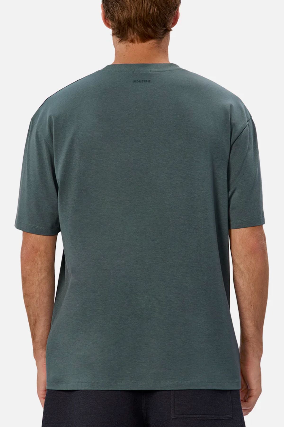 A man is seen from behind wearing the Industrie The Freeman Athletic Tee in dark teal and black shorts, set against a plain light background.