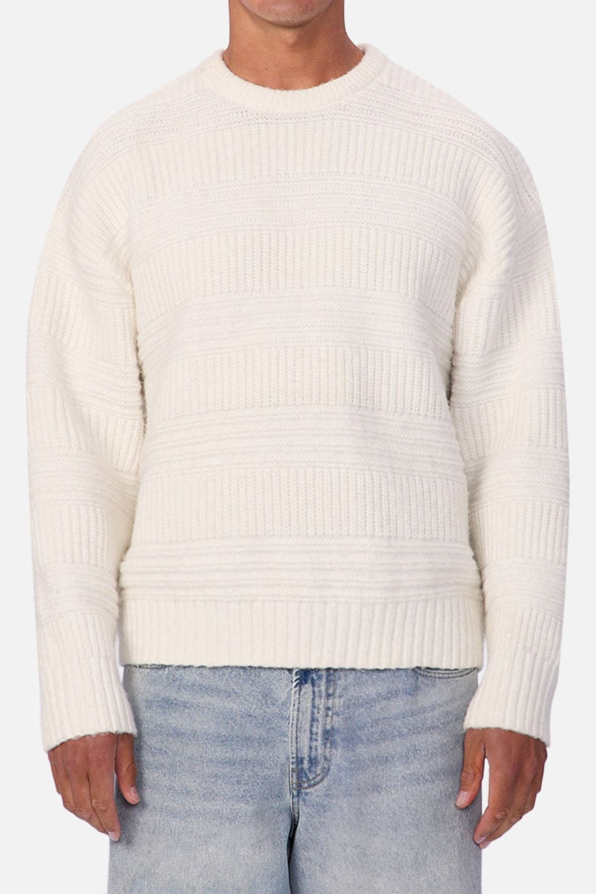 Someone wearing the Industrie The Huntington Knit in off-white with a textured pattern and light blue jeans stands against a plain light background.