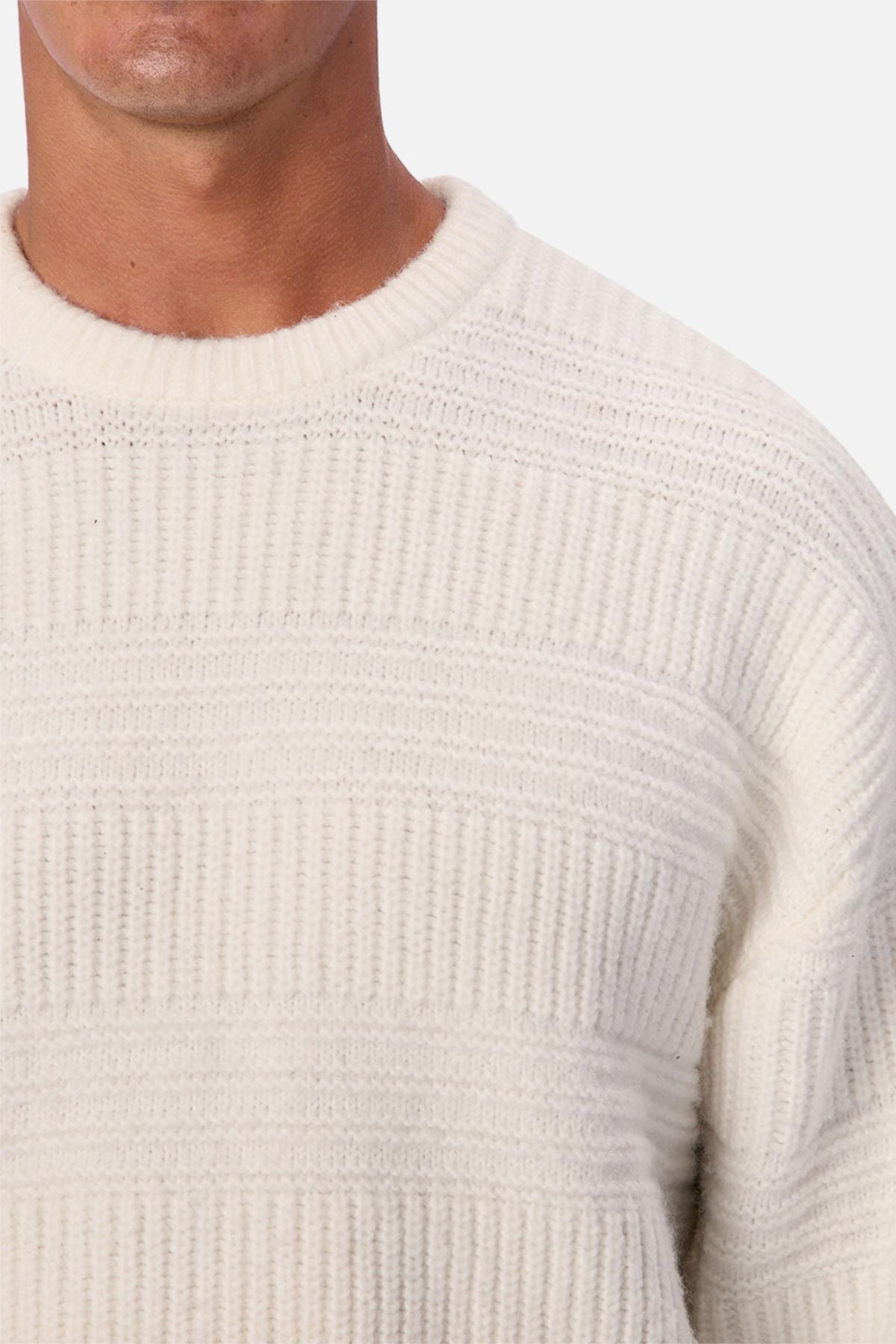 A close-up of a person wearing the Industrie The Huntington Knit, featuring a textured, off-white ribbed pattern. Only the lower half of the face, neck, and upper torso are visible.