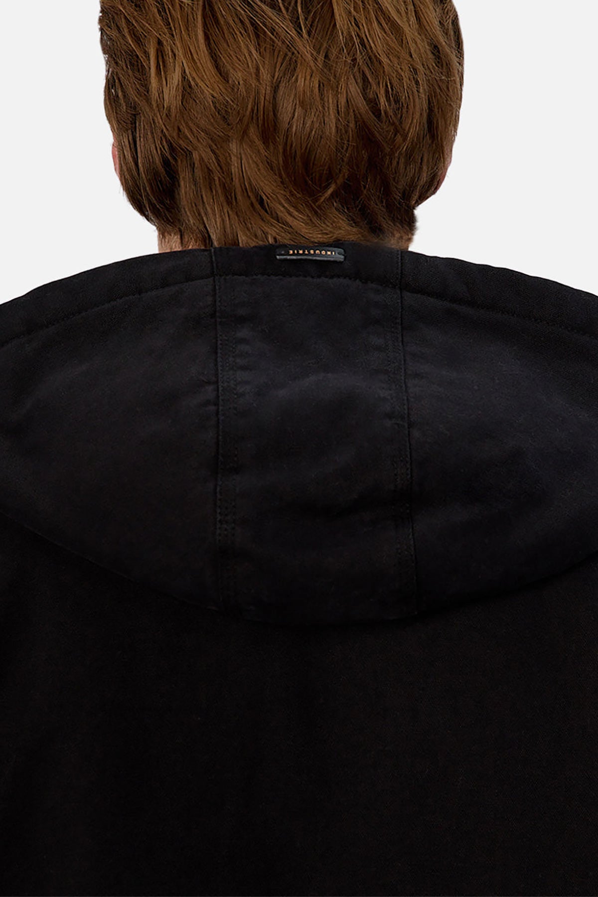 A person with light brown hair is seen from behind wearing the Industrie The Illinois Jacket, a black hoodie featuring a small black label by the neckline and showcasing its heavyweight construction.