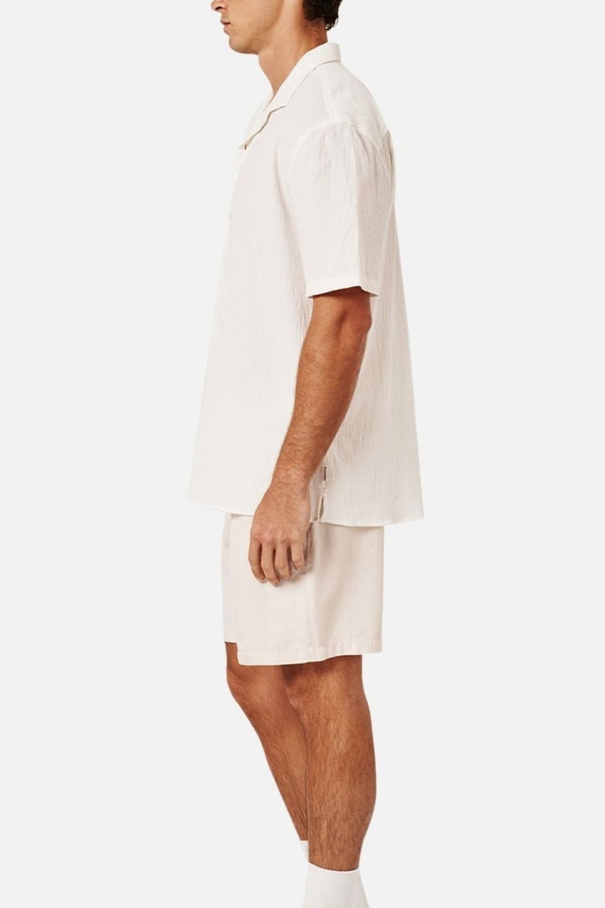 A man with short hair is shown in left profile, wearing the Industrie The Magna Short Sleeve Shirt and matching cream-colored shorts. The breathable shirt features an oversized, loose fit. He stands sideways against a plain white background.