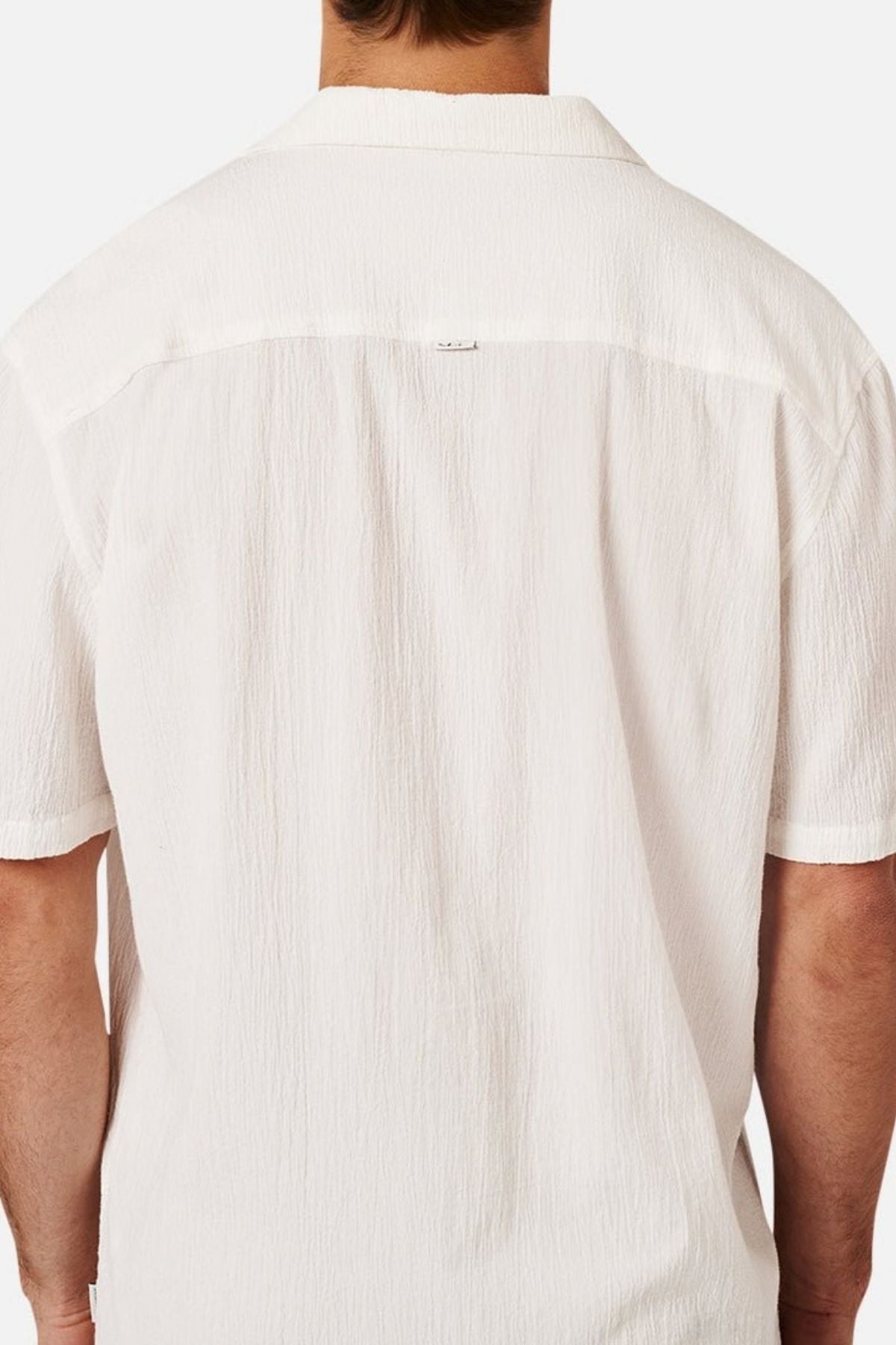 A person is shown from behind wearing the Industrie The Magna Short Sleeve Shirt, a white textured short-sleeve style. Only the upper back and arms are visible, and the plain, light-colored background emphasizes the shirt’s oversized fit.