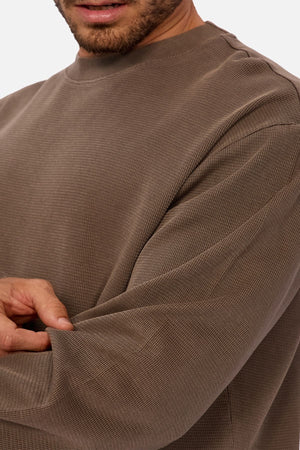 A man in the Industrie The Marlon Long Sleeve Tee, made from 100% cotton, adjusts his sleeve. The image emphasizes the tee’s versatile design, capturing his torso and upper arm with his face partially visible.