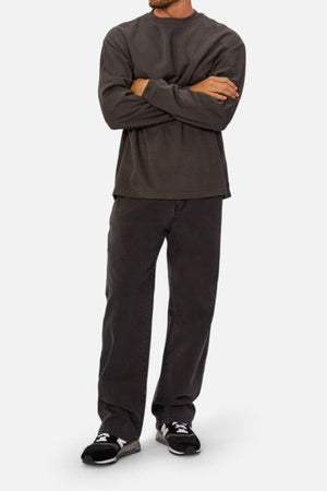 A person with arms crossed wears a loose dark gray Industrie The Marlon Long Sleeve Tee (100% cotton), matching pants, and black sneakers with white soles. Head not visible. Background is plain light gray.