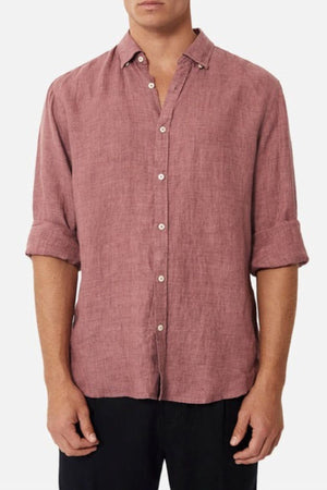 A person wearing the mauve Industrie The Midland Shirt, recognized for its INDUSTRIE branding, with rolled-up sleeves and black pants, stands against a plain white background.