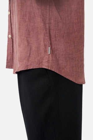 A person in a maroon Industrie The Midland Shirt and black pants stands sideways. The linen shirt includes a small INDUSTRIE branding label on the side.