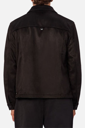 A person is seen from the back wearing the Industrie The Monaco Jacket in black, featuring a collar, long lined sleeves, a lined torso, and a small rectangular tag at the upper back, paired with black pants for a stylish look.