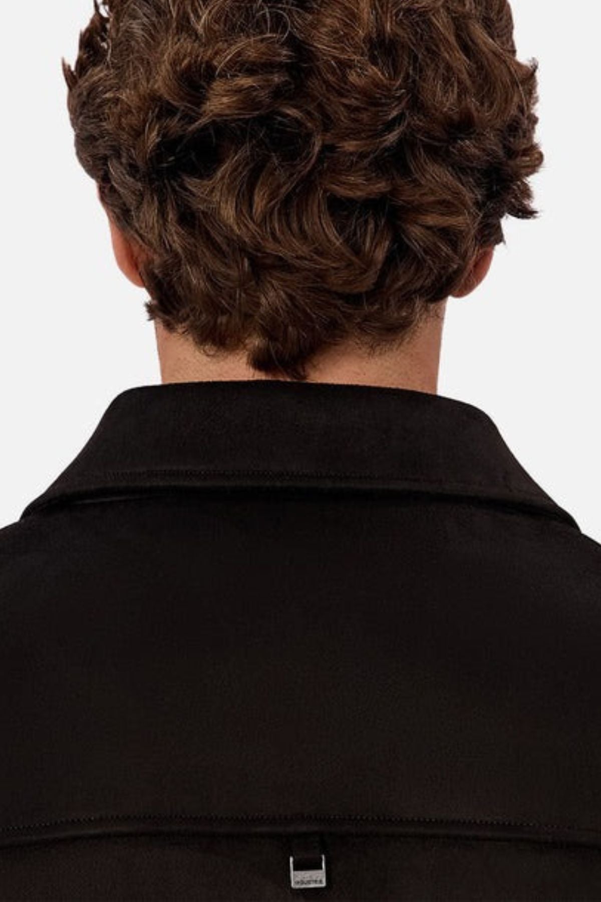 The image shows the back view of a person with short, curly brown hair wearing the Industrie The Monaco Jacket, a versatile black collared jacket that offers both comfort and style. The background is plain white.