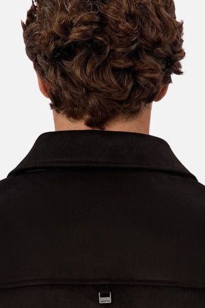 The image shows the back view of a person with short, curly brown hair wearing the Industrie The Monaco Jacket, a versatile black collared jacket that offers both comfort and style. The background is plain white.