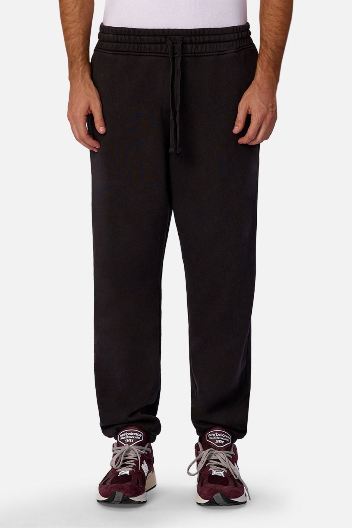 A person wearing Industrie The New Del Sur Trackpant in black, paired with a white shirt and maroon sneakers, stands against a plain light background. Only the lower half of the body is visible.