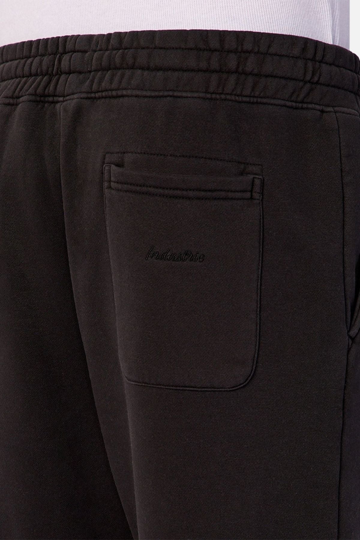 Close-up of the back pocket area of Industrie The New Del Sur Trackpant in black, featuring an elastic waistband, relaxed fit, and subtle embroidered text on the pocket. Worn by a person in a white shirt.