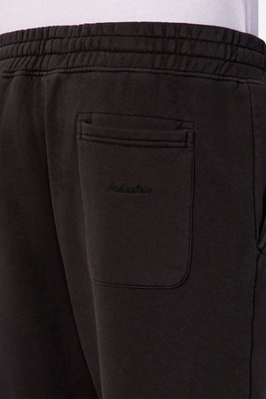 Close-up of the back pocket area of Industrie The New Del Sur Trackpant in black, featuring an elastic waistband, relaxed fit, and subtle embroidered text on the pocket. Worn by a person in a white shirt.