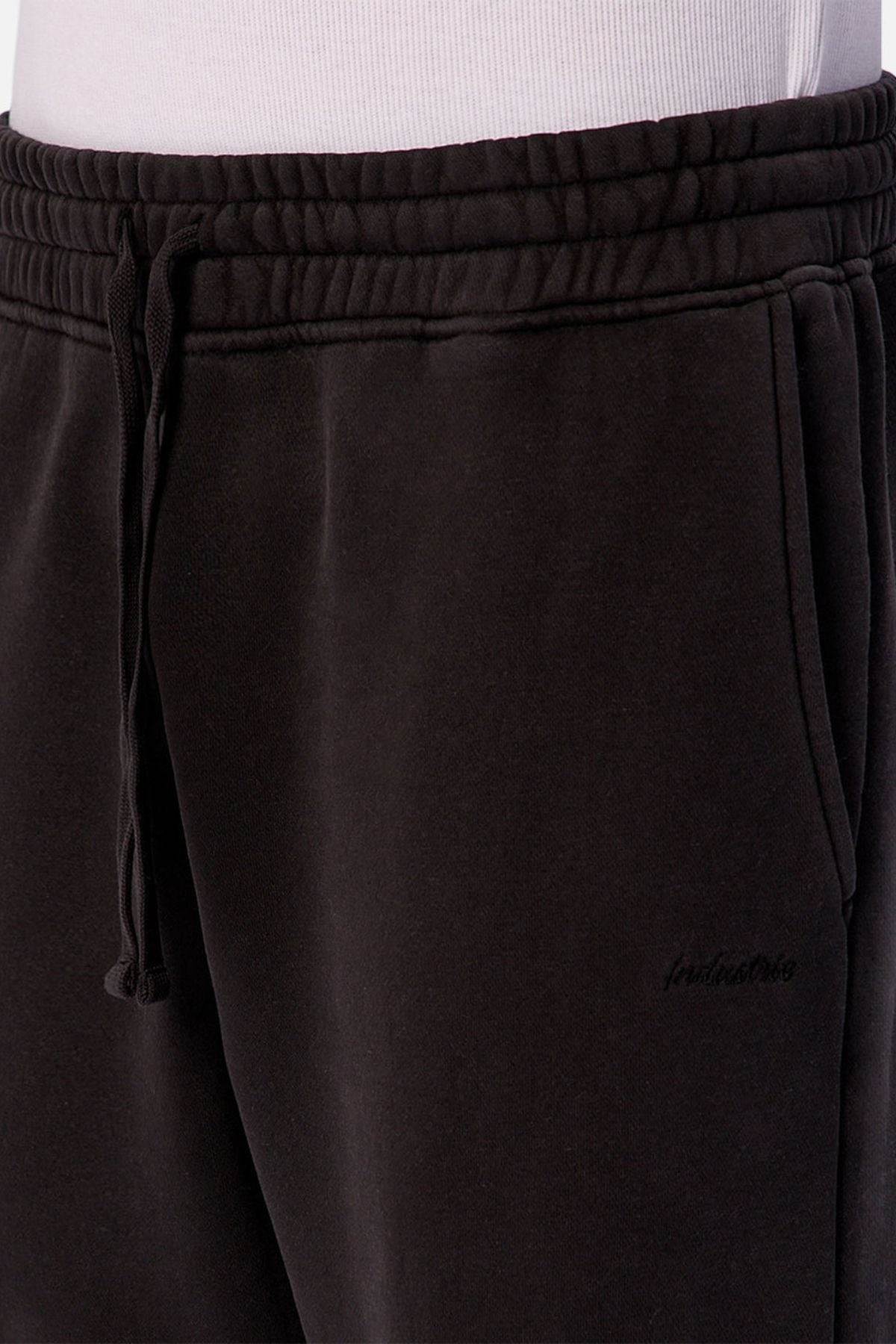 Close-up of a person wearing Industrie The New Del Sur Trackpant in black with a relaxed fit and visible waistband, paired with a white shirt—ideal men's loungewear.