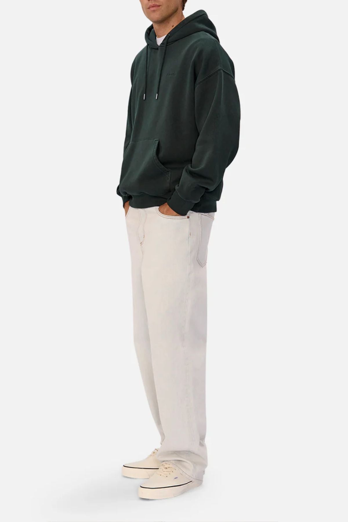 Someone wears an oversized Industrie The New Del Sur Washed Hoodie in dark green, with hands in the front pocket, loose-fitting light beige pants, and off-white sneakers, standing against a plain white background.