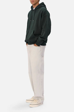 Someone wears an oversized Industrie The New Del Sur Washed Hoodie in dark green, with hands in the front pocket, loose-fitting light beige pants, and off-white sneakers, standing against a plain white background.