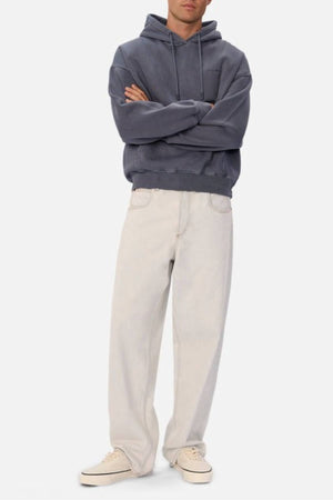 A person stands with arms crossed, wearing the Industrie The New Del Sur Washed Hoodie in an oversized fit, loose light beige jeans, and cream sneakers against a plain white background.