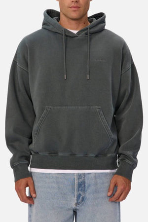 A person wears the Industrie The New Del Sur Washed Hoodie in dark gray, featuring an oversized fit and front pocket, styled with light blue jeans, shown from the waist up against a plain background.