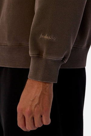 A close-up of a hand and arm wearing Industrie The New Del Sur Washed Sweat with the Industrie logo on the cuff, highlighting its oversized fit. It’s paired with black pants against a plain white background.