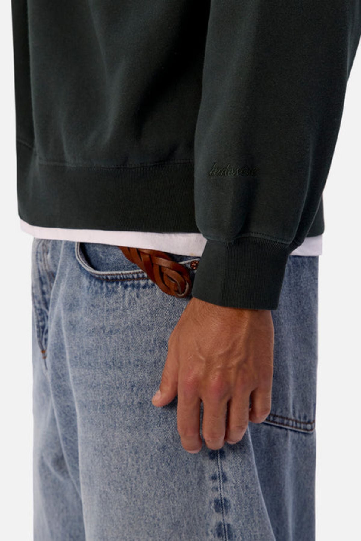 A person wears an oversized Industrie The New Del Sur Washed Sweat over a white shirt, paired with light blue jeans and a brown braided belt. Only their torso and right hand are visible.