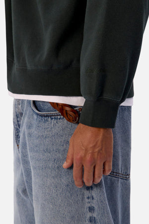 A person wears an oversized Industrie The New Del Sur Washed Sweat over a white shirt, paired with light blue jeans and a brown braided belt. Only their torso and right hand are visible.