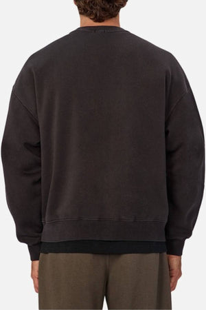 A person is seen from the back in an oversized Industrie The New Del Sur Washed Sweat and brown pants. The image highlights the upper body, emphasizing the roomy silhouette and subtle Industrie logo on the sweatshirt.