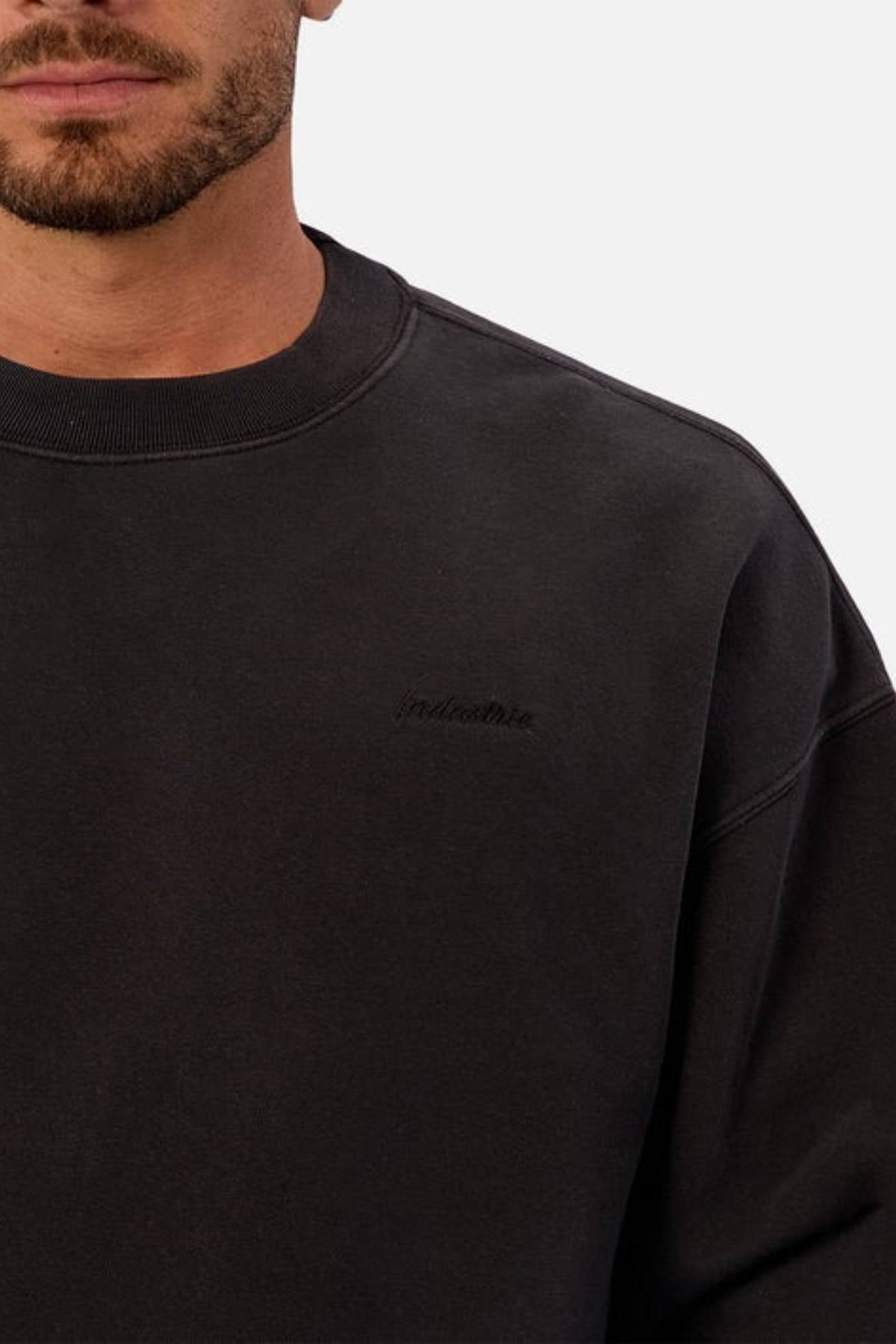 A man wears the Industrie The New Del Sur Washed Sweat, a black crewneck with subtle embroidery and an oversized fit. Shown from the shoulders up, his face is partially out of frame against a plain light background.