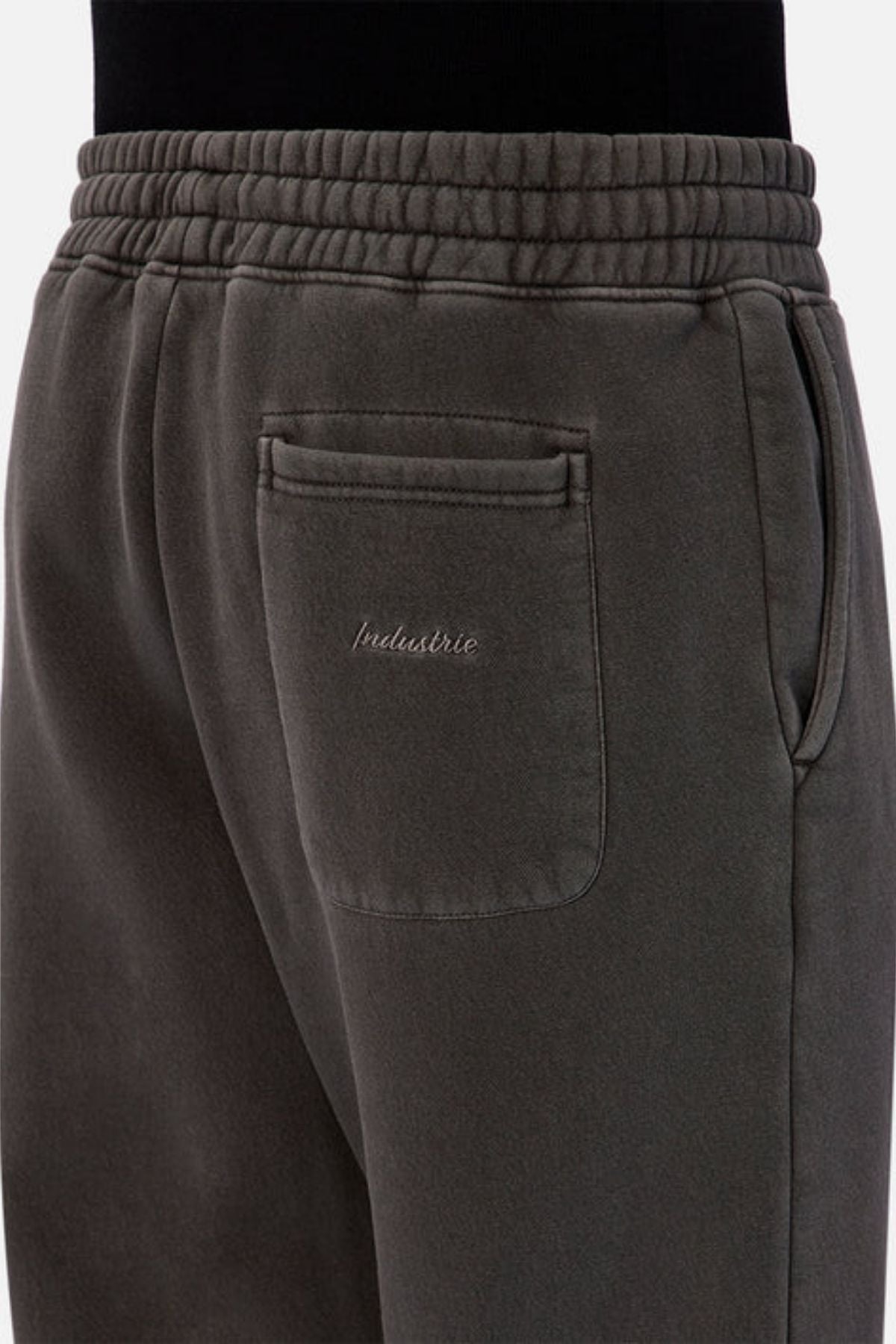 Close-up of the back pocket on the Industrie The New Del Sur Washed Trackpant in dark grey, featuring the INDUSTRIE logo embroidered above the pocket, worn by a person in black.