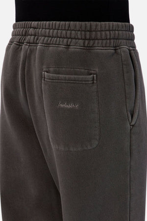 Close-up of the back pocket on the Industrie The New Del Sur Washed Trackpant in dark grey, featuring the INDUSTRIE logo embroidered above the pocket, worn by a person in black.