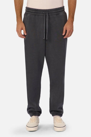 Someone wears the Industrie The New Del Sur Washed Trackpant in dark gray, featuring a drawstring and elastic waist. Paired with a light shirt and white sneakers, it creates an easy, oversized-fit look with hands in pockets.