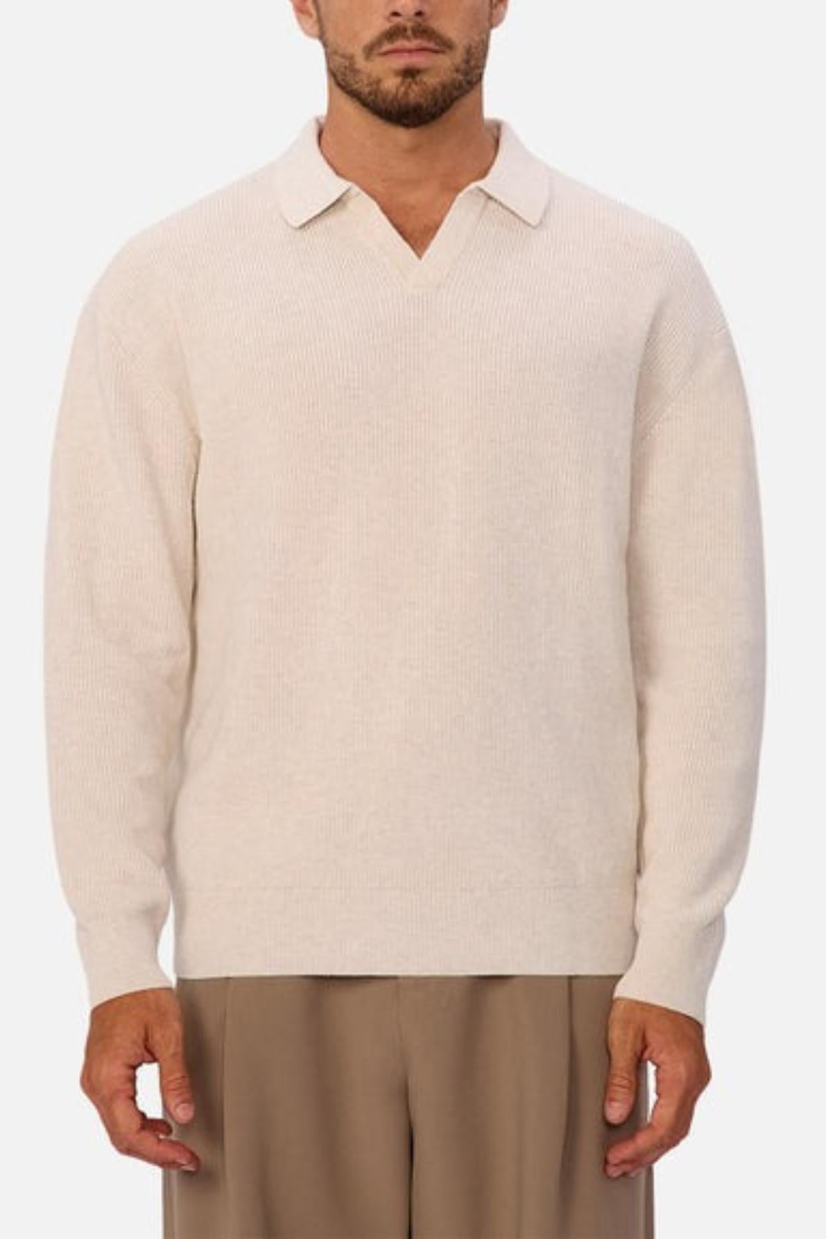 A man wears the Industrie The New England Polo Knit in light beige, featuring a soft collar and V-neck, paired with light brown trousers, standing against a plain white background.