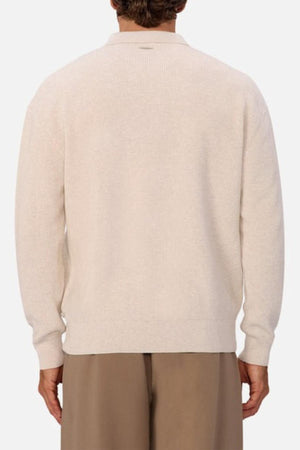 A person is shown from the back wearing the Industrie The New England Polo Knit, a light beige long-sleeve sweater, paired with loose brown pants against a plain light background.