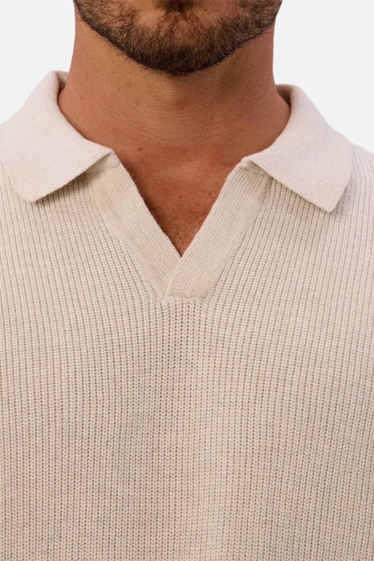 Close-up of a person wearing the Industrie The New England Polo Knit in beige, featuring soft ribbed knit fabric and an open collar. Only the lower face, neck, and upper chest are visible against a plain white background.