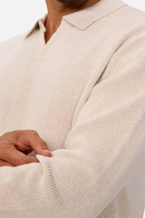 A person folds their arms wearing the Industrie The New England Polo Knit in light beige, made from high-quality 100% cotton knit fabric. The image highlights the shirt's texture and detail of their arms.
