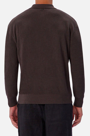 A person is seen from the back wearing an Industrie The New England Polo Knit, a dark brown ribbed long-sleeve 100% cotton sweater, with black pants against a plain light gray background.