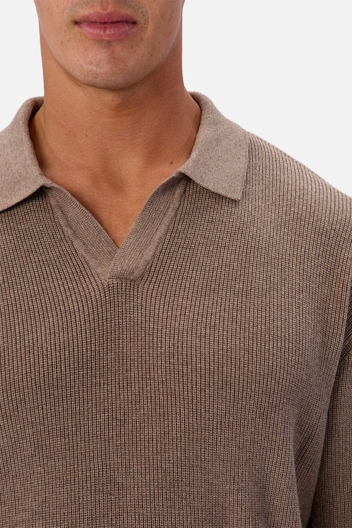 A person wears the Industrie The New England Polo Knit, a ribbed, light brown V-neck sweater made from 100% cotton. Shown from lower face to upper chest against a plain white background.