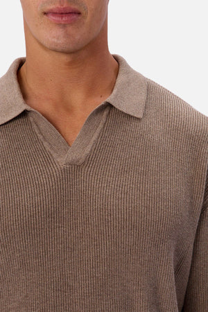 A person wears the Industrie The New England Polo Knit, a ribbed, light brown V-neck sweater made from 100% cotton. Shown from lower face to upper chest against a plain white background.