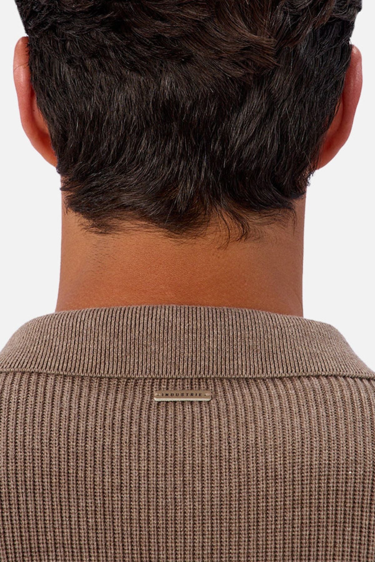 A close-up of the back of a personโs neck and head with short dark hair, wearing Industrie The New England Polo Knitโa ribbed brown 100% cotton polo featuring a small rectangular metallic tag below the collar.
