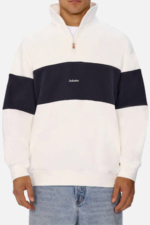 A person wears the Industrie The New Luton Track Top, a white men's track top with a wide black stripe, modern panelled design, “Industrie” embroidered on the chest, paired with light blue jeans.
