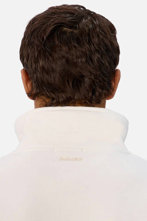 A person with short brown hair is shown from behind, wearing the Industrie The New Luton Track Top—a white men’s track top with a modern paneled design and subtle embroidered collar text—against a plain, light background.
