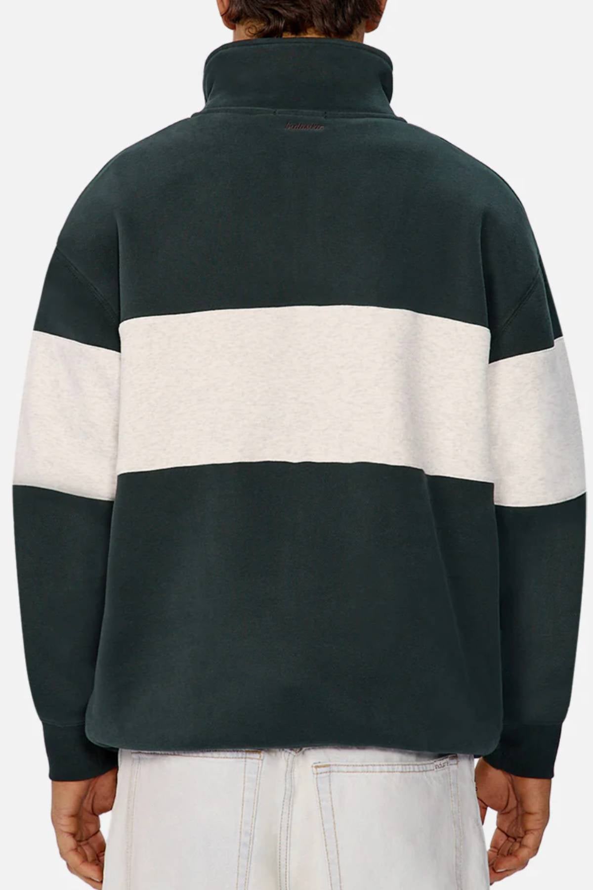 A person is seen from the back wearing Industrie The New Luton Track Top in relaxed fit dark green with a thick white stripe and high collar, paired with light-wash jeans for a casual look.