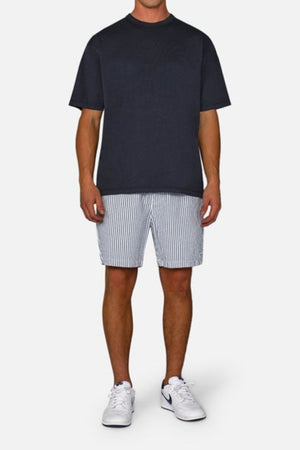 A person stands against a plain background wearing a black T-shirt and the Industrie The New Southwest Short, which features white and blue vertical stripes along with an elasticated waistband. Paired with white sneakers, the outfit exudes a casual and relaxed vibe.