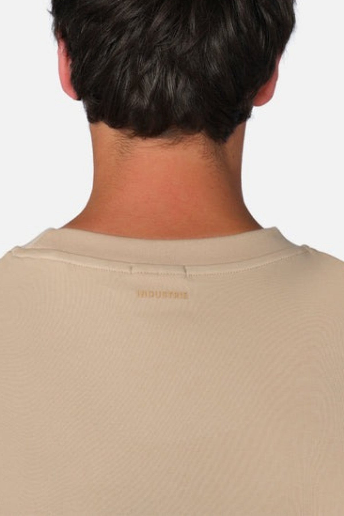 Rear view of a person with short, dark hair wearing the Industrie The Newport Tee in beige. The image highlights the back of their head and neck, showcasing the texture and color of the 100% cotton fabric in an oversized fit. Subtle yet distinct, the Industrie branded logo adds a touch of finesse.